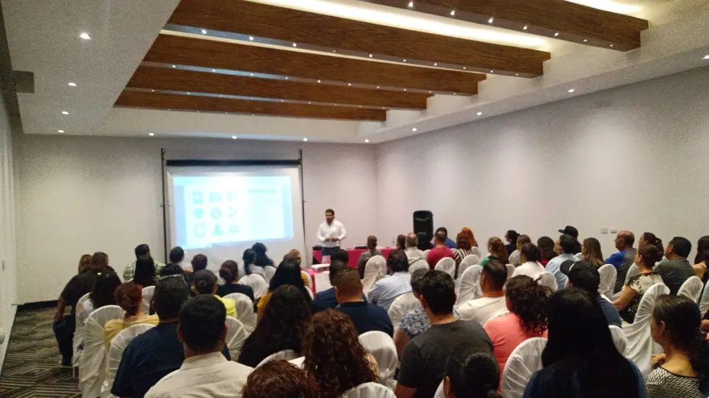 Junta informativa de MATIE con papás en un salón, con la presentación en pantalla