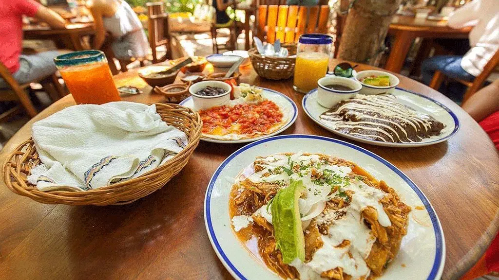 Mesa con desayuno mexicano: chilaquiles, enmoladas, huevos a la mexicana y jugo
